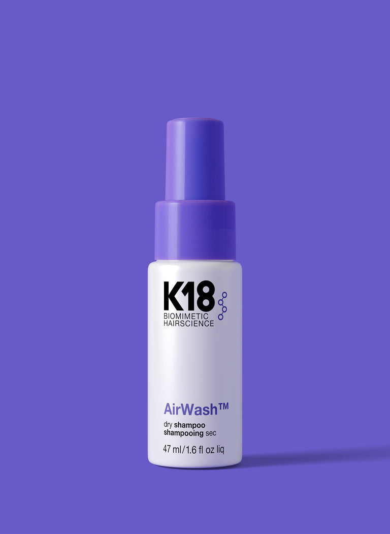 A spray bottle of Mini AirWash dry shampoo against a purple background.