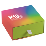 A medium-sized gift box with a colorful gradient design and a green drawer with a silver handle. The box is labeled with the brand 'K18'.