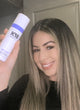 woman with blonde hair holding dry shampoo bottle.