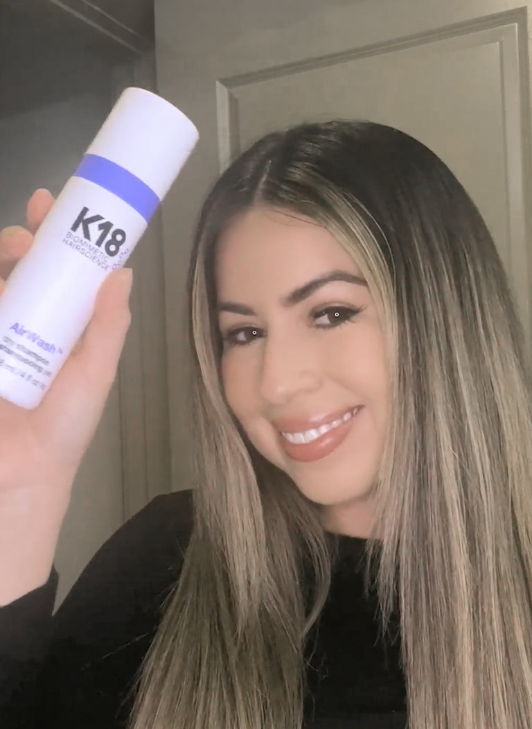 woman with blonde hair holding dry shampoo bottle.